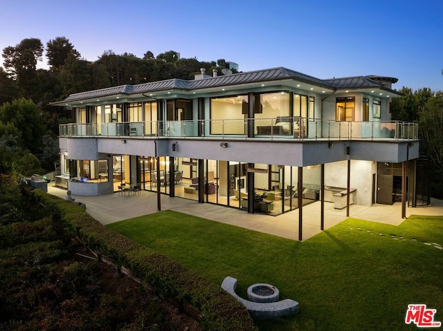 back house at dusk with a patio area, a balcony, and a yard