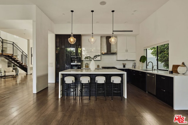 kitchen with hanging light fixtures, white cabinets, wall chimney range hood, and a center island