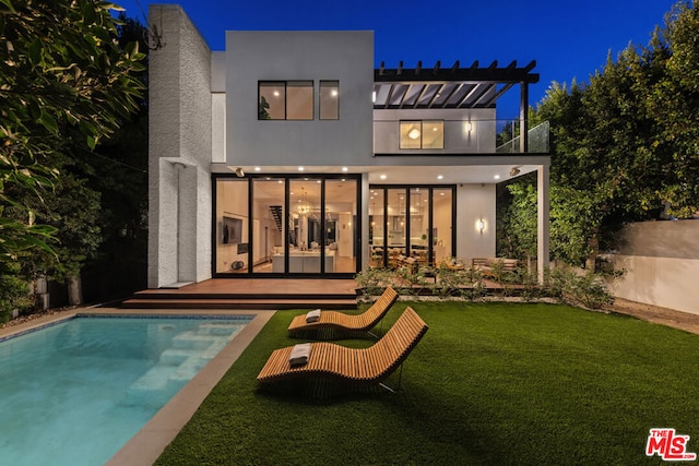 back house at twilight with a pool side deck, a balcony, and a yard