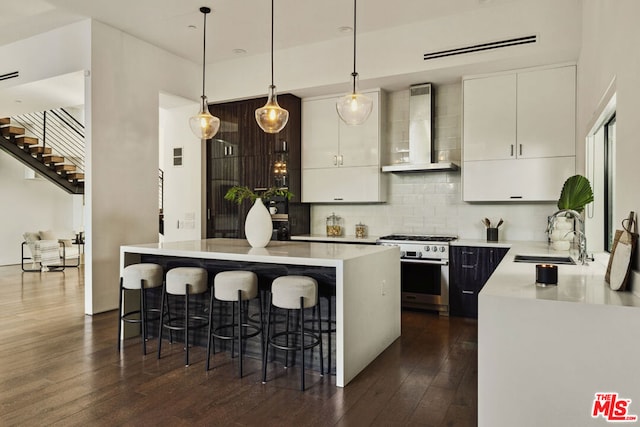 kitchen featuring a center island, decorative light fixtures, wall chimney range hood, stainless steel stove, and sink