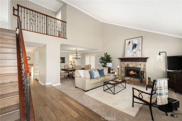 living room featuring a towering ceiling, crown molding, hardwood / wood-style flooring, an inviting chandelier, and a stone fireplace