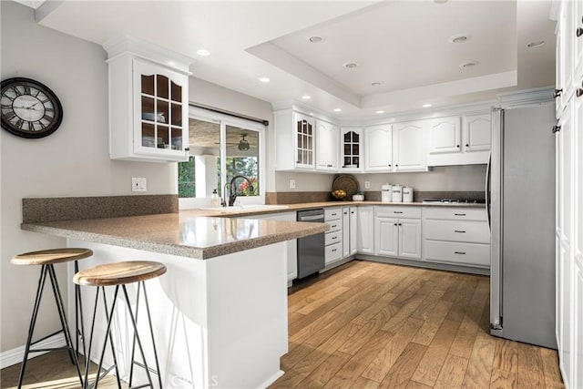 kitchen featuring a kitchen breakfast bar, kitchen peninsula, appliances with stainless steel finishes, white cabinets, and light wood-type flooring