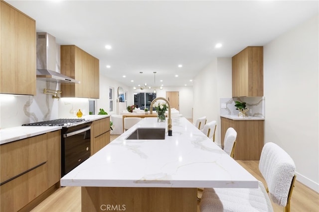 kitchen featuring sink, wall chimney exhaust hood, a kitchen breakfast bar, light hardwood / wood-style flooring, and a large island with sink