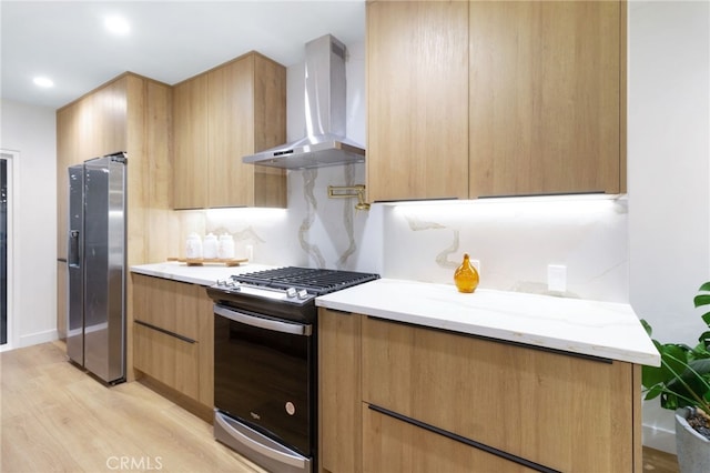 kitchen featuring light wood-type flooring, light stone countertops, wall chimney exhaust hood, and appliances with stainless steel finishes