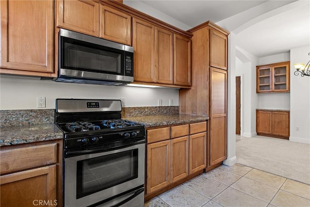 kitchen with light tile patterned floors, stainless steel appliances, dark stone counters, and a notable chandelier