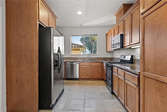 kitchen featuring dark stone counters, sink, light tile patterned floors, and stainless steel appliances