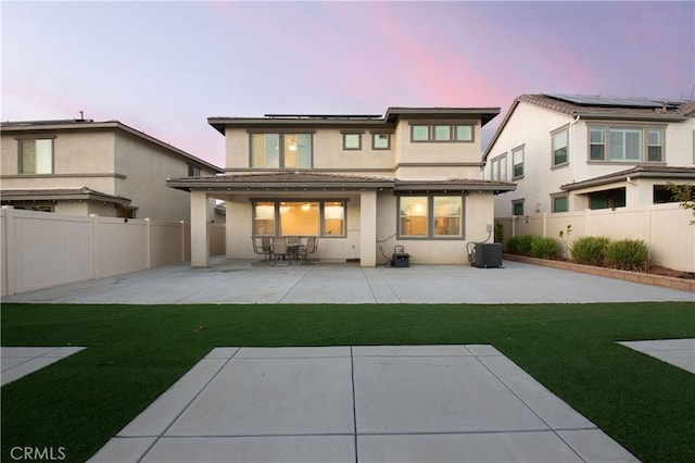 back house at dusk with cooling unit, a patio area, and a yard