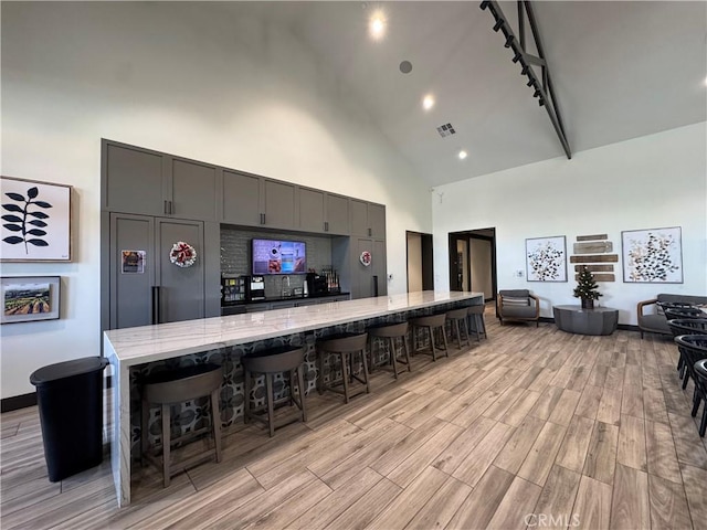 kitchen featuring gray cabinetry, light hardwood / wood-style flooring, high vaulted ceiling, track lighting, and a kitchen bar