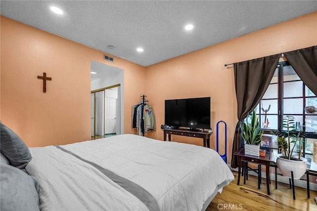 bedroom with light hardwood / wood-style floors, a textured ceiling, a baseboard heating unit, and a closet