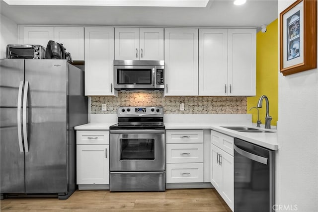 kitchen with white cabinets, sink, appliances with stainless steel finishes, tasteful backsplash, and light hardwood / wood-style floors