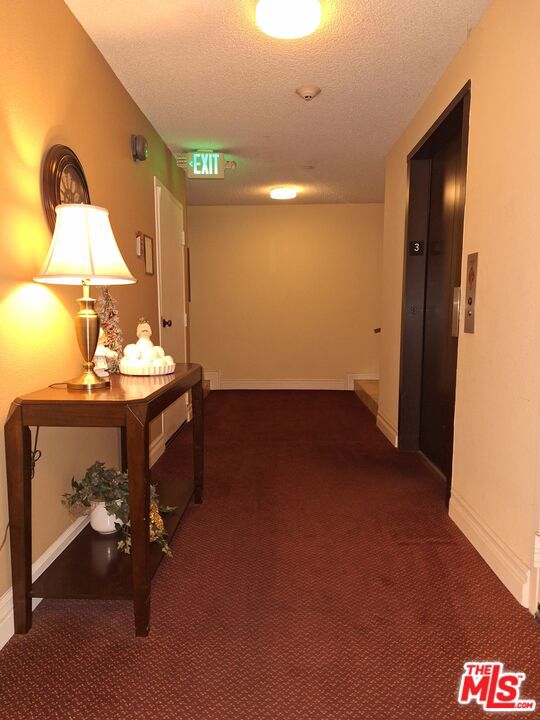 hall featuring a textured ceiling, dark colored carpet, and elevator