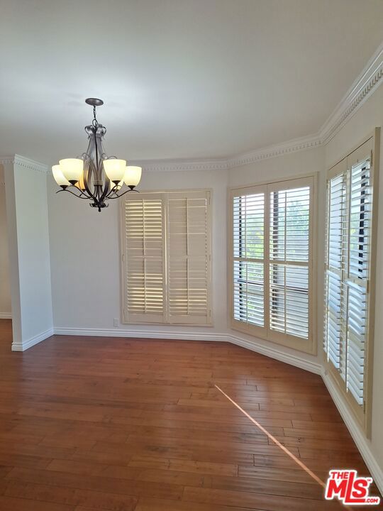 unfurnished room featuring dark wood-type flooring, ornamental molding, and a notable chandelier