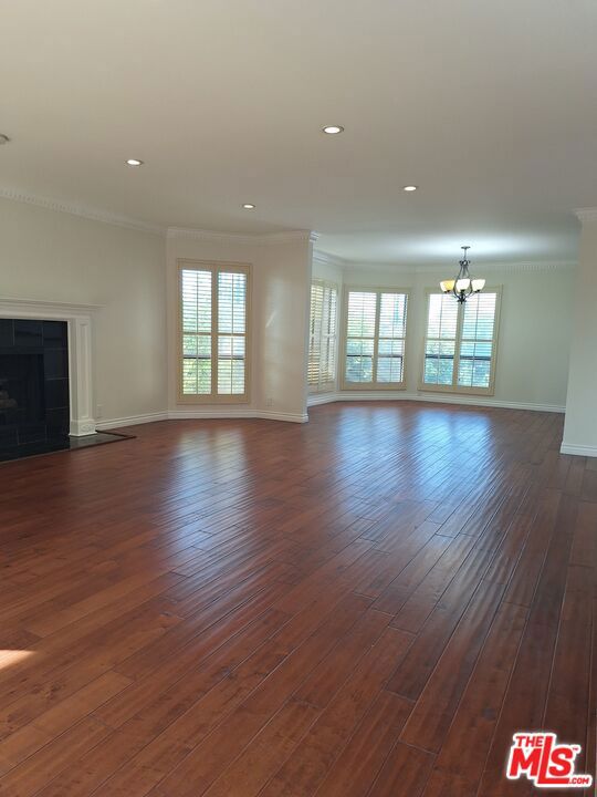 unfurnished living room featuring a fireplace, dark hardwood / wood-style floors, crown molding, and a chandelier