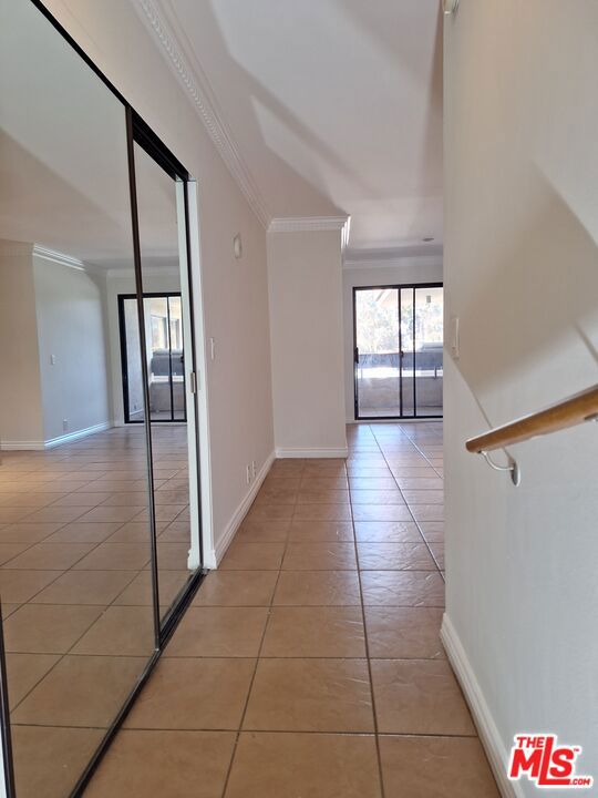 hall featuring light tile patterned floors and crown molding