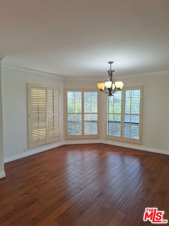 empty room featuring dark wood-type flooring, ornamental molding, and an inviting chandelier