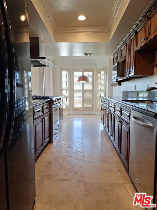 kitchen with appliances with stainless steel finishes, a raised ceiling, wall chimney range hood, pendant lighting, and dark brown cabinetry