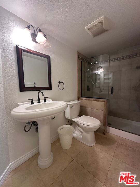 bathroom with walk in shower, tile patterned floors, toilet, and a textured ceiling