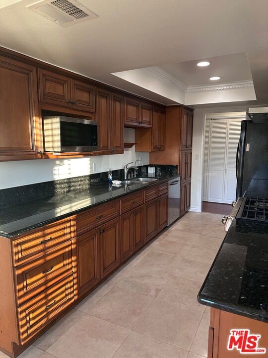 kitchen featuring dark stone countertops, a raised ceiling, sink, stainless steel appliances, and ornamental molding