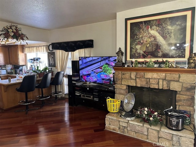 living area featuring a textured ceiling, a stone fireplace, and wood finished floors