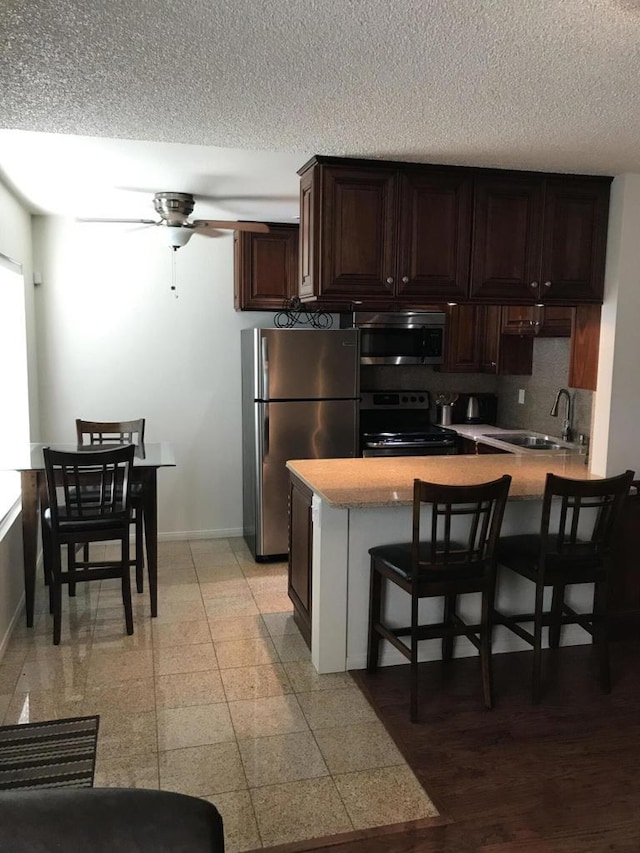 kitchen with ceiling fan, sink, stainless steel appliances, a kitchen breakfast bar, and kitchen peninsula