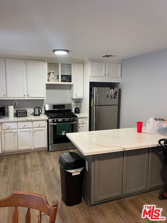 kitchen featuring white cabinets, light stone counters, wood-type flooring, and stainless steel appliances