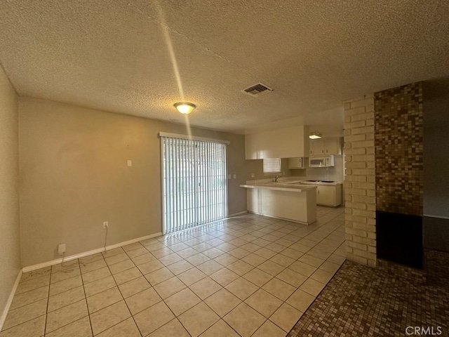 kitchen with kitchen peninsula, white cabinets, light tile patterned flooring, and a textured ceiling