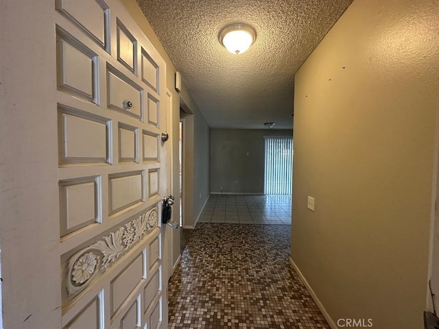 hall with a textured ceiling and dark tile patterned flooring