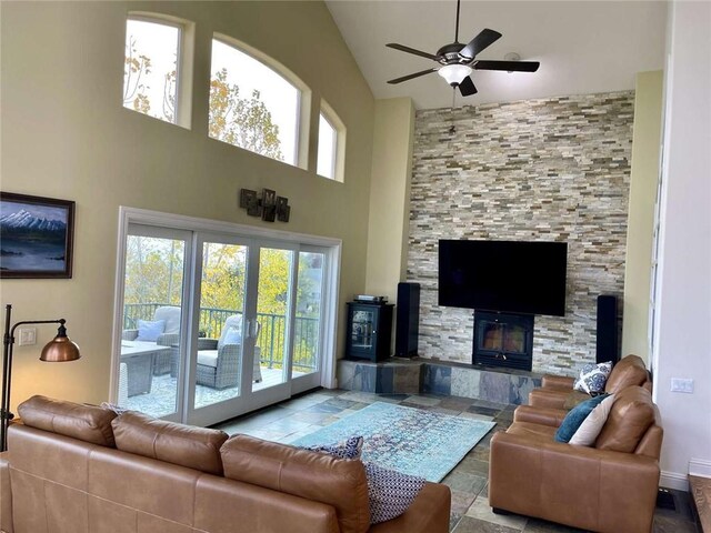 living room with ceiling fan, a stone fireplace, and high vaulted ceiling