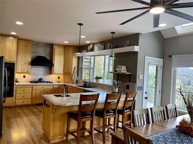 kitchen with black appliances, sink, hanging light fixtures, light wood-type flooring, and kitchen peninsula