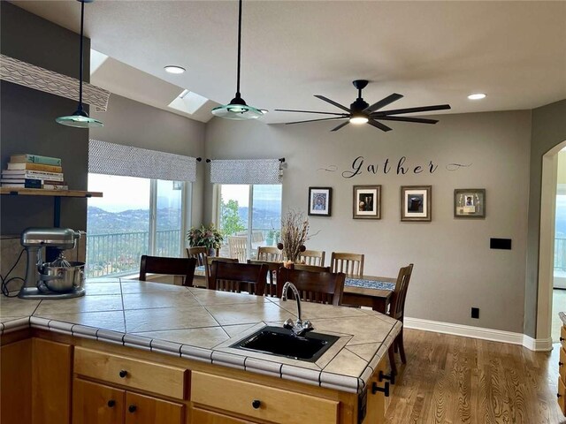 kitchen with sink, a skylight, dark hardwood / wood-style floors, ceiling fan, and tile counters