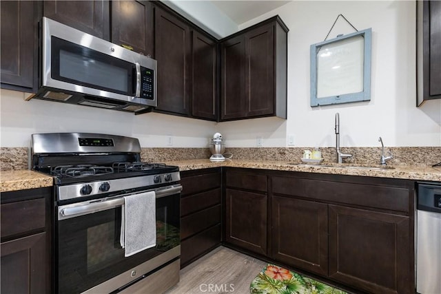 kitchen with sink, light wood-type flooring, light stone counters, dark brown cabinetry, and stainless steel appliances