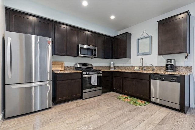 kitchen with light stone countertops, sink, dark brown cabinets, appliances with stainless steel finishes, and light wood-type flooring