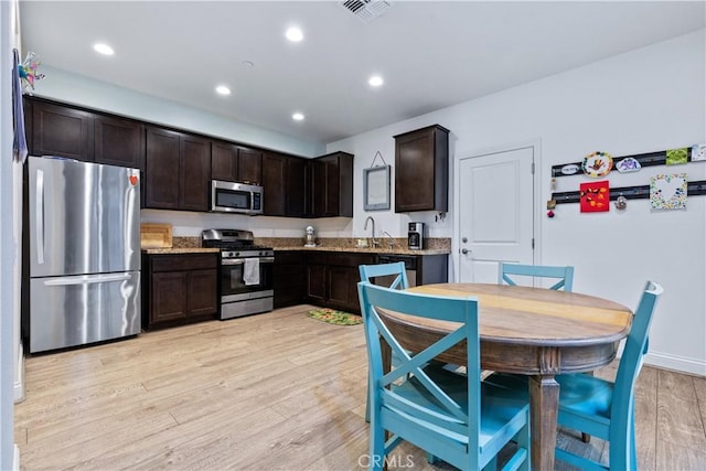 kitchen featuring dark brown cabinetry, light stone countertops, sink, light hardwood / wood-style flooring, and appliances with stainless steel finishes