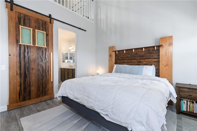 bedroom with connected bathroom, a towering ceiling, wood-type flooring, and a barn door