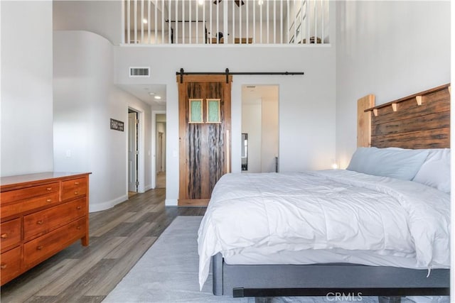 bedroom with a high ceiling, a barn door, and hardwood / wood-style floors