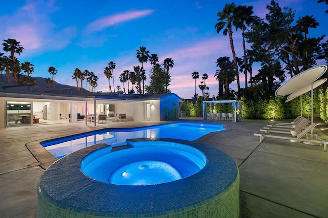 pool at dusk featuring a patio area and an in ground hot tub