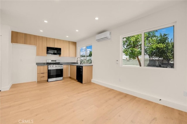 kitchen with sink, light brown cabinets, a wall unit AC, light hardwood / wood-style floors, and black appliances