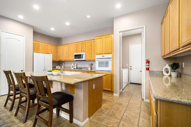 kitchen with light stone countertops, a breakfast bar, white appliances, sink, and light tile patterned floors