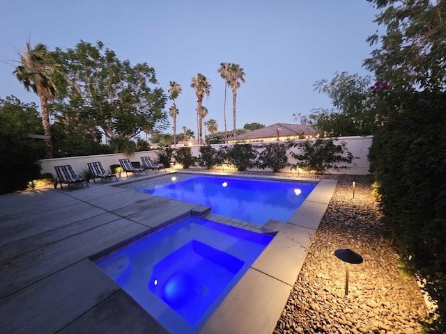 pool at dusk featuring an in ground hot tub and a patio area