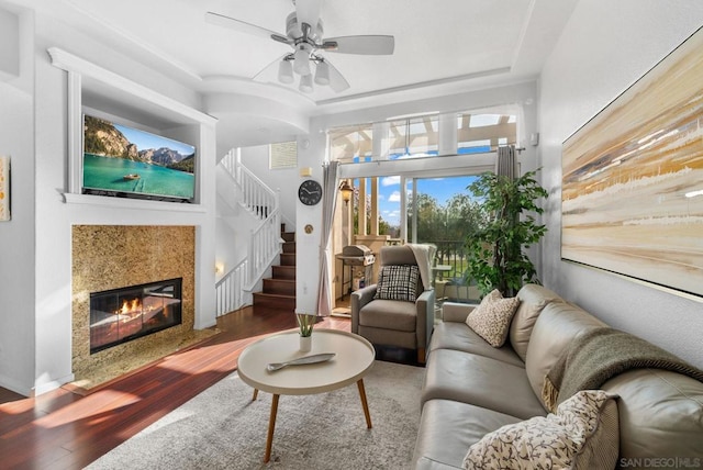 living room featuring hardwood / wood-style flooring, a premium fireplace, ceiling fan, and a tray ceiling