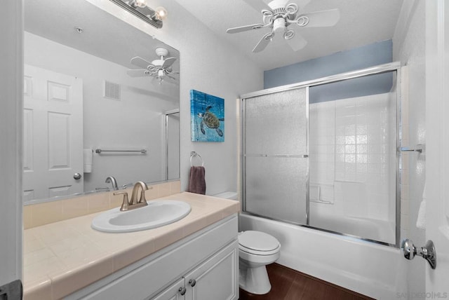 full bathroom featuring combined bath / shower with glass door, wood-type flooring, vanity, ceiling fan, and toilet