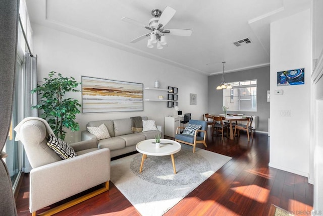 living room featuring ceiling fan with notable chandelier and dark wood-type flooring