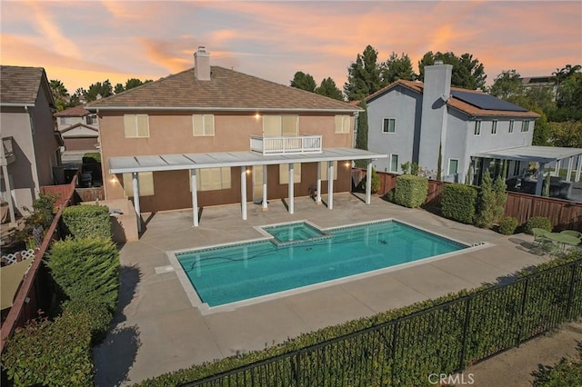 back house at dusk featuring a swimming pool with hot tub, a balcony, and a patio area