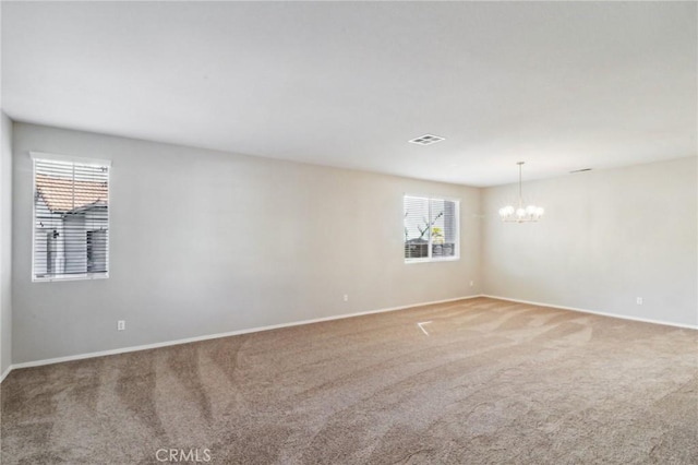 carpeted spare room featuring a healthy amount of sunlight and an inviting chandelier