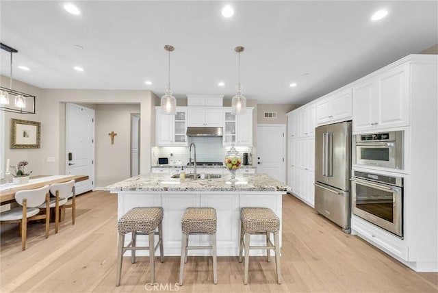 kitchen with light wood-type flooring, stainless steel appliances, sink, pendant lighting, and white cabinetry