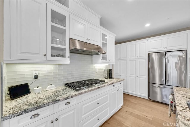 kitchen featuring tasteful backsplash, light stone counters, stainless steel appliances, light hardwood / wood-style flooring, and white cabinets