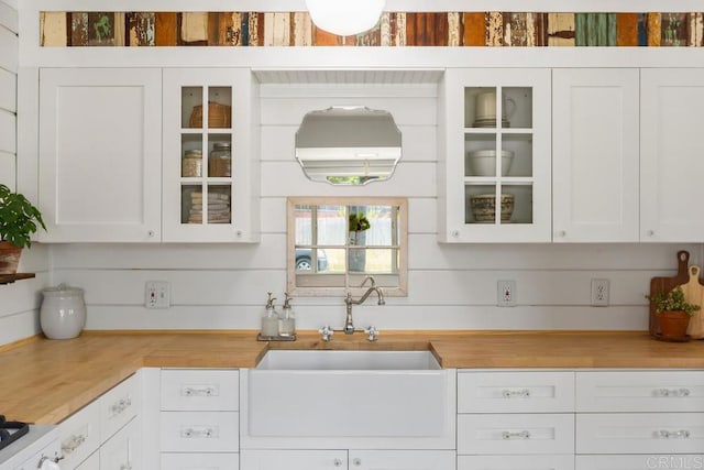 kitchen featuring a sink, glass insert cabinets, white cabinets, and wooden counters