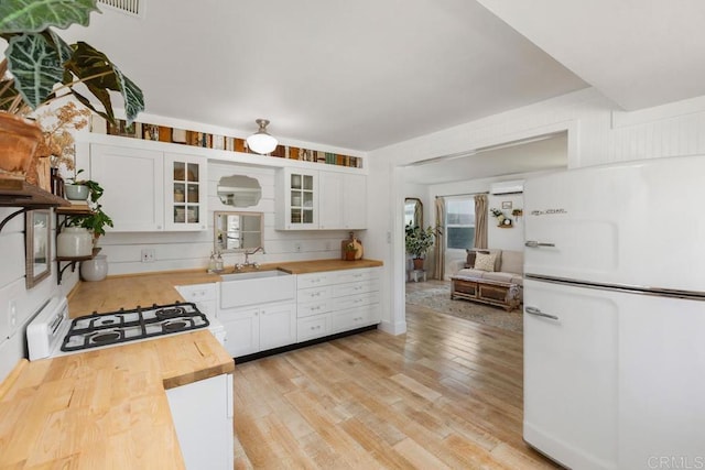 kitchen featuring butcher block countertops, a sink, light wood finished floors, and white appliances