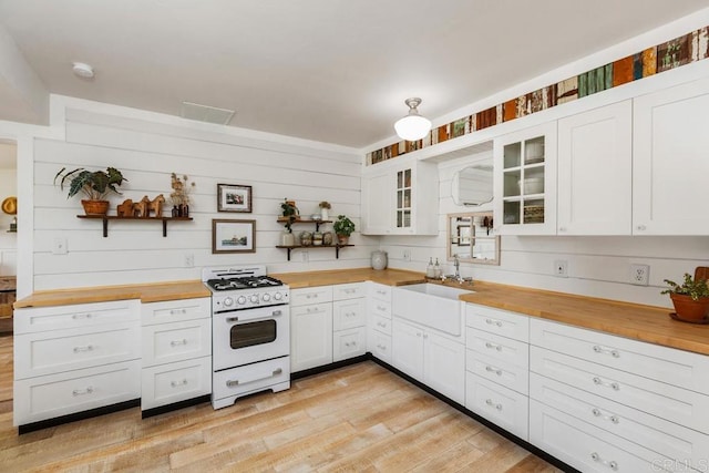 kitchen featuring open shelves, butcher block countertops, a sink, and white gas range