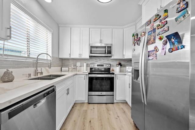 kitchen with sink, tasteful backsplash, appliances with stainless steel finishes, white cabinets, and light wood-type flooring